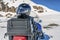 Snowmobile safety helmet lays at the luggage trunk mounted on backside of blue snowmobile, close up view. Blurry mountains covered