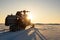 A snowmobile stands on the snow at sunset.