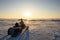 A snowmobile stands on the snow at sunset.