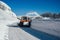 A snowplow truck removing snow from a winding rural road on sunny winter day