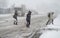 A snowstorm in the city. People cross the snowy road in front of cars