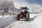 After the snowstorm, a tractor diligently clears the road, creating a passage.