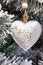 Snowy branch of christmas tree with white heart shape decoration on rustic style.White heart on snow encrusted fir tree