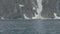 Snowy cliff on rocky island. View from ship sailing past snowy mountain and cliff