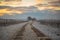 Snowy curvy path with two tracks through the vineyards at sunset. White vineyards with cloudy orange sky. Calming evening mood in