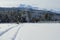 Snowy field and car tracks on forest road with sunshine and mountain backdrop