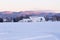 Snowy field with white barns seen during an early sunny winter morning with the Laurentian mountains