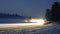 Snowy foggy forest road with trails from car lights.