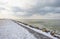 Snowy iced rocks of a dike along a white frozen lake in wetland under a blue cloudy sky in winter