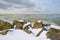 Snowy iced rocks of a dike along a white frozen lake in wetland under a blue cloudy sky in winter