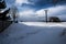 A snowy landscape with a cross under a tree and a pole with an electric lead