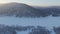 A snowy landscape with frozen water, trees, and mountains viewed from above