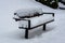 Snowy landscape. The park bench is covered with white thick snow. Winter day
