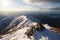 snowy mountaintop, with view of sunlit valley below, and surrounding peaks in the distance