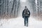 Snowy path in a winter forest, a lonely man with a backpack and a ski pole on a walk, rear view