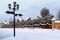 Snowy road between country houses. Winter landscape with street lamp, street signs, sidewalk, snow footprints. Street landscape