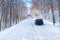 Snowy road in winter forest with single car