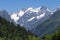 Snowy rocky mountains peaks and forest on blue sky background on sunny summer day. Caucasus mounts. Mountain landscape.