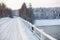 Snowy surface of empty country road on bridge across a river, winter season