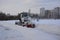 Snowy tractor of a municipal service throws the snow from walkways in city park on winter morning