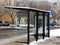 snowy urban road in the winter. modern glass and aluminum bus shelter in urban setting. parked cars.