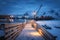 Snowy wooden pier on the sea coast with lights, houses and boats