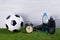 Soccer ball, a bottle of water, black boots and an alarm clock stand on the grass, on a gray background