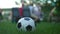 Soccer ball on green grass with group of blurred children sitting at table at background. Sports equipment on summer