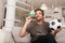 Soccer fan man watching football game on television at living room couch. He holds a credit card and a digital tablet for