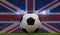 Soccer football ball on a grass pitch in front of stadium lights and UK flag. 3D Rendering