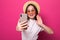 Sociable asian young girl taking selfie or speaking on video call using cell phone isolated over pink background