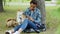 Sociable girl is using smartphone texting friends and stroking her adorable puppy while resting in park at weekend