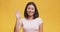 Sociable young asian woman smiling friendly at camera and waving hand gesturing hello, yellow background