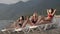 Social distancing. Multiracial female friends in protective face mask sunbathing on public beach. New life after