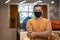 Social distancing at work. Portrait of young confident man, male office worker in protective face mask keeping arms