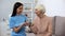 Social worker assisting old woman making exercise with dumbbell, rehabilitation