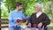 Social worker reading book for disabled pensioner, leisure in park, volunteering