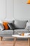 Sofa with pillows and a coffee table with an orange in a living room interior. Real photo