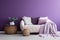 Sofa and pouf covered with blanket against purple wall with copy space. Minimalist interior design of modern living room