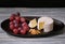 Soft blue cheese, ripe red grapes and walnuts on black dish, aperitif for wine