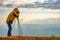 Soft blur image of photographer look through the camera with tripod and point to the mountain over the cliff with morning light