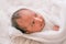 Soft blurred image of Asian newborn baby cover by white cloth on white bed and smile to show emotion of relax and happy