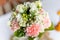 Soft bridal bouquet of fresh flowers and wedding gold rings on celebratory table closeup, blurred background. Elegant