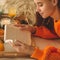 Soft cozy photo of woman in warm orange sweater on the bed with cup of tea and fruit. Girl sitting on the bed with old books.