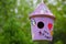 Soft focus of a purple, wooden birdhouse against blurry greenery