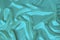 Soft folds on delicate turquoise shining silk, luxury concept, background for the designer, horizontal, close-up, copy space