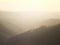 Soft hillside tree covered valley landscape blurred by fog at sunrise glowing a warm orange color with the tops of hills showing