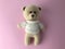 Soft knitted bear on a pink matte background. bear for a gift, a toy for children. knitted bear, beige. bear is made of natural