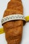 Soft measuring ruler wrapped around a croissant as a symbol of unhealthy nutrition