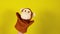 Soft puppet toy on hand on yellow background. Concept of puppet show. Close-up of hand with puppet monkey.